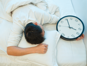 A man sleeping on his stomach in a bed next to a black and white wall clock