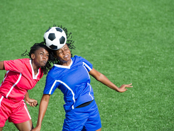 Two soccer players hitting the ball with their head