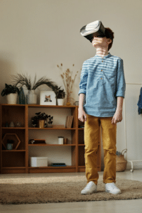 A boy in a blue striped shirt and yellow pants wearing a virtual reality headset
