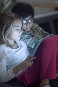 Un niño y una niña sentados en un autocar viendo un vídeo en su tableta