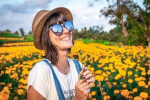 woman wearing sunglasses and a hat while smiling in a field of flowers