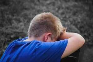 A sad child in a blue shirt leaning against a bench