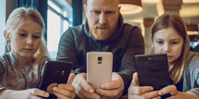 A father and his two children staring at their smartphone screens