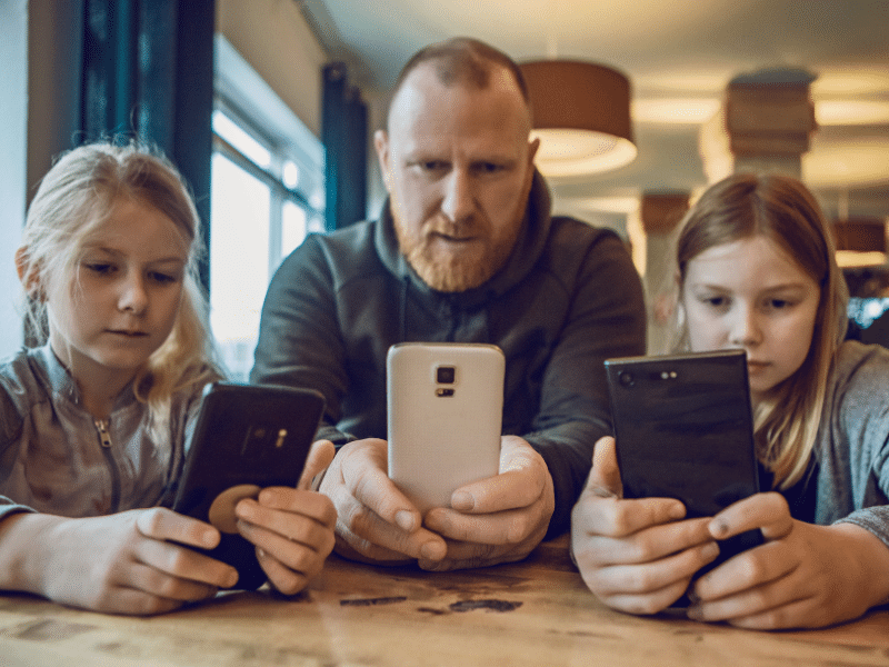Un padre y sus dos hijos miran las pantallas de sus smartphones