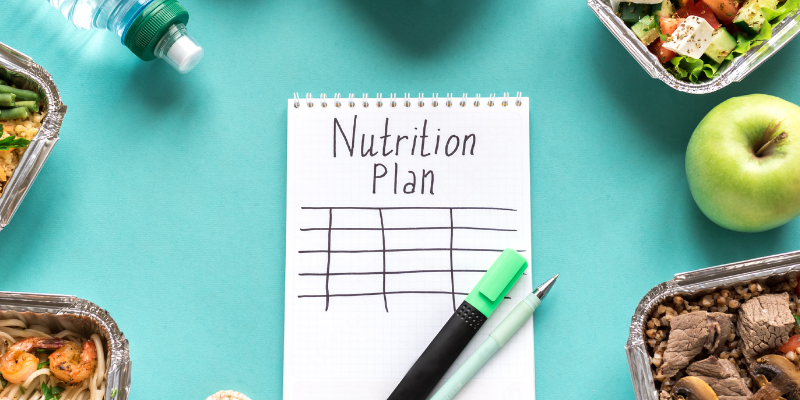 Un cuaderno con la etiqueta "Plan de nutrición" rodeado de comidas saludables