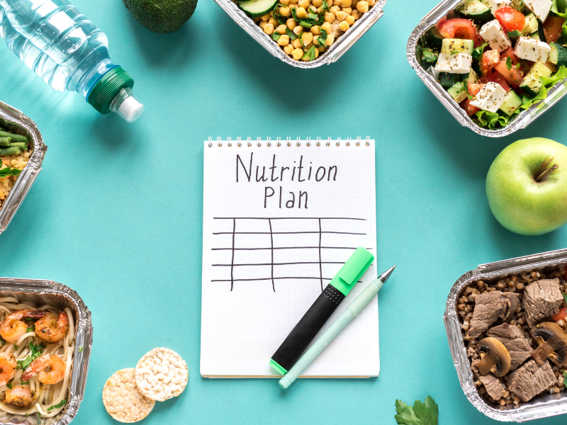 Un cuaderno con la etiqueta "Plan de nutrición" rodeado de comidas saludables