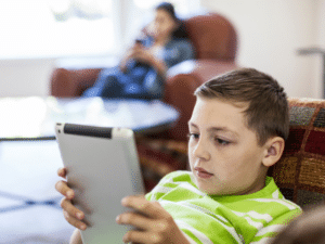 A child using a mobile tablet while his mother uses a smartphone in the background